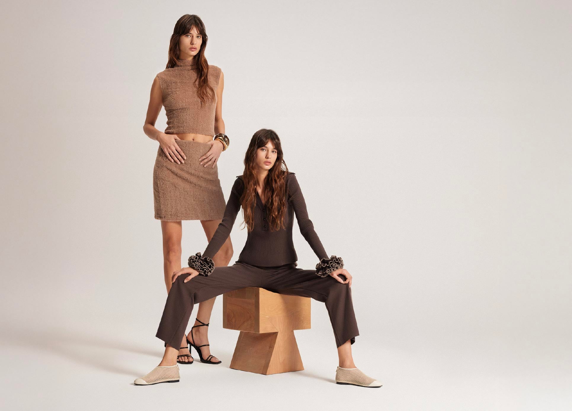 Two women in brown and black outfits posing against a white background